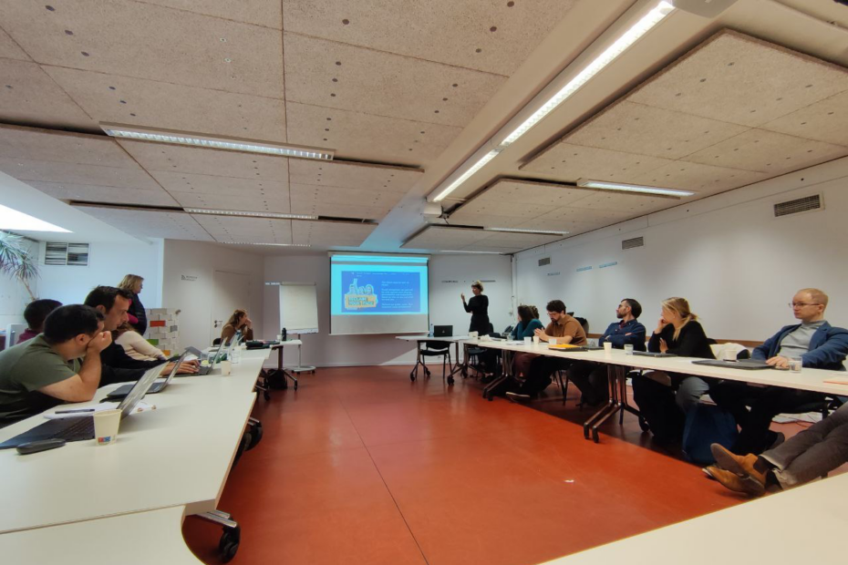 Communications workshop. People sitting around a large table and looking at a presentation.